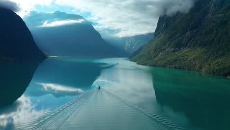 white clouds and towering forest-covered mountains reflected in the still turquoise waters of the loenvatnes lake