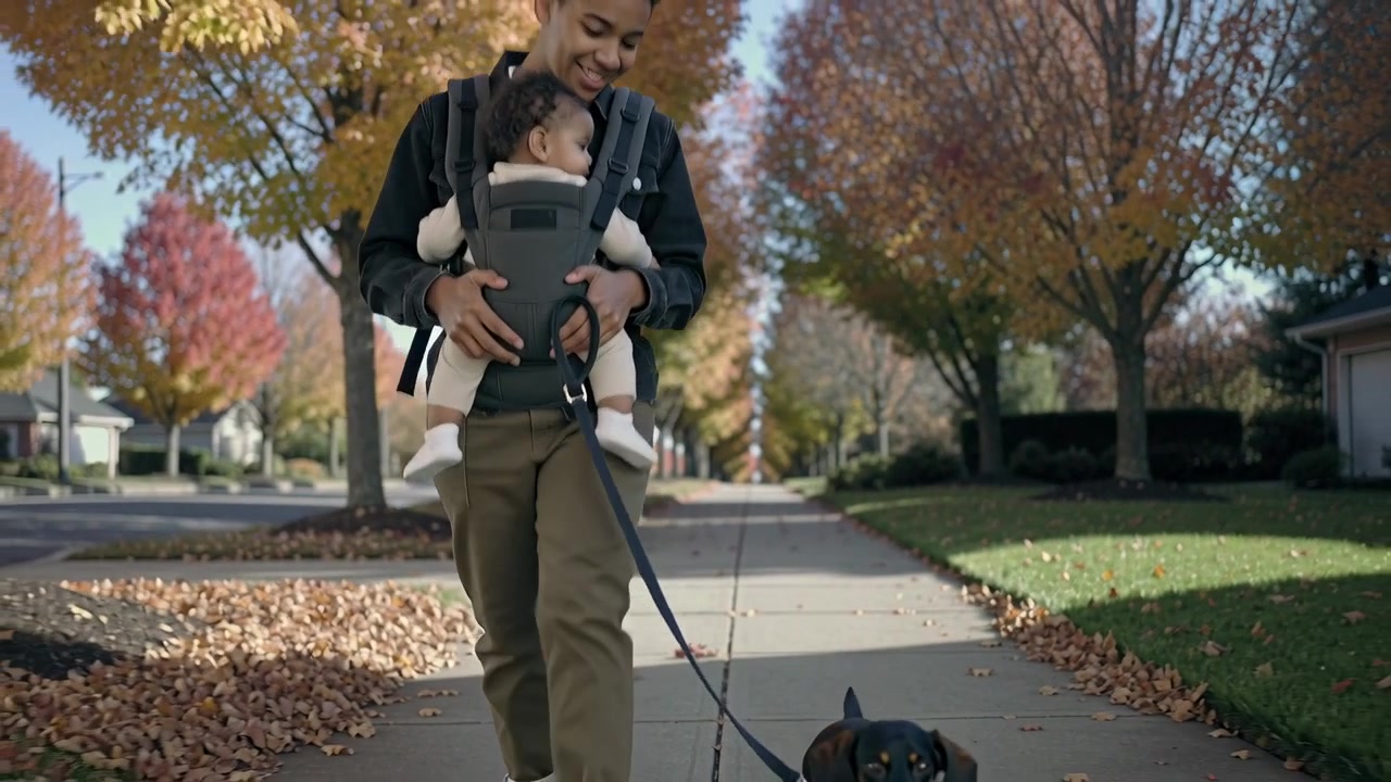 Stepping forward, caregiver in hoodie carrying baby in front carrier on sidewalk