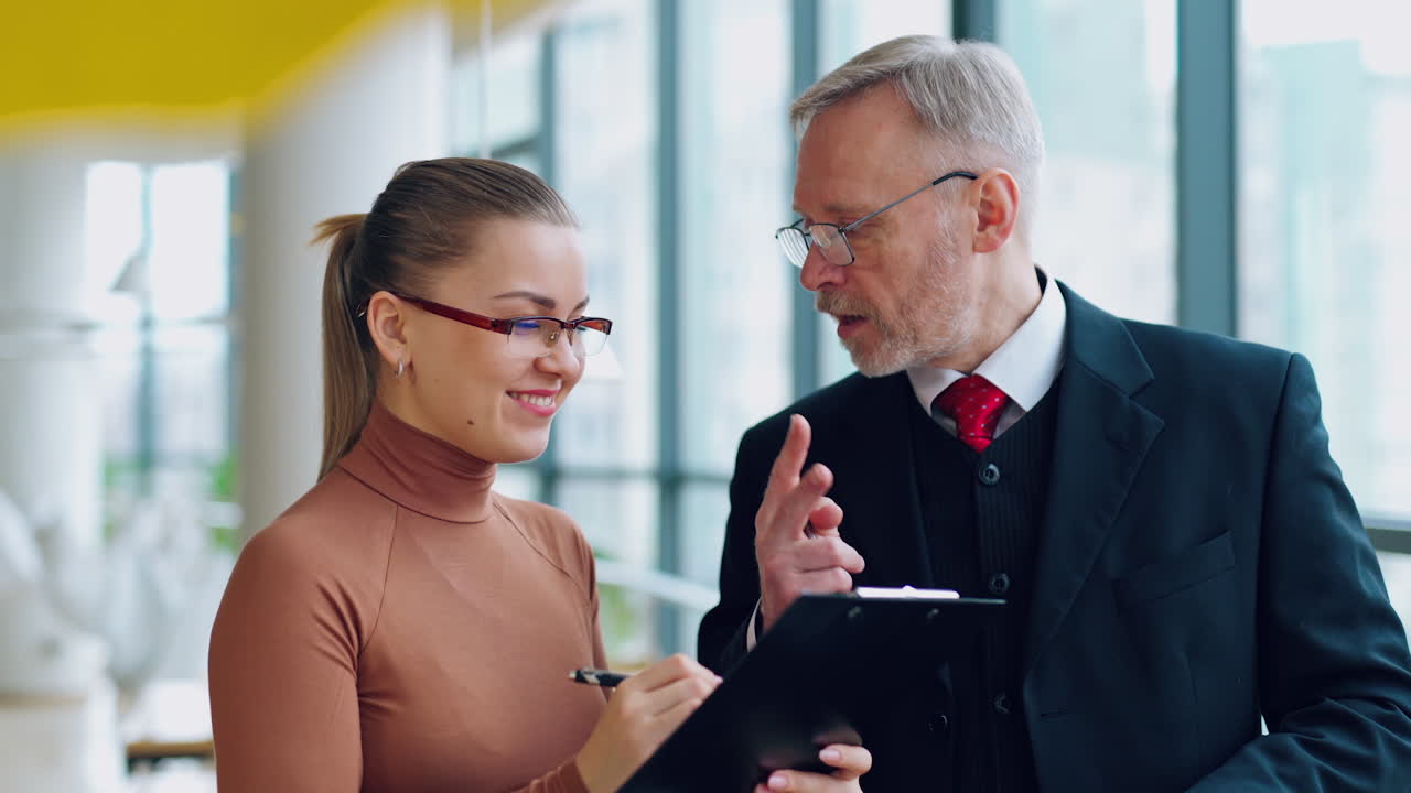 Smiling old businessman and a female secretary. Young woman talking with a mature man in costume in the modern office.