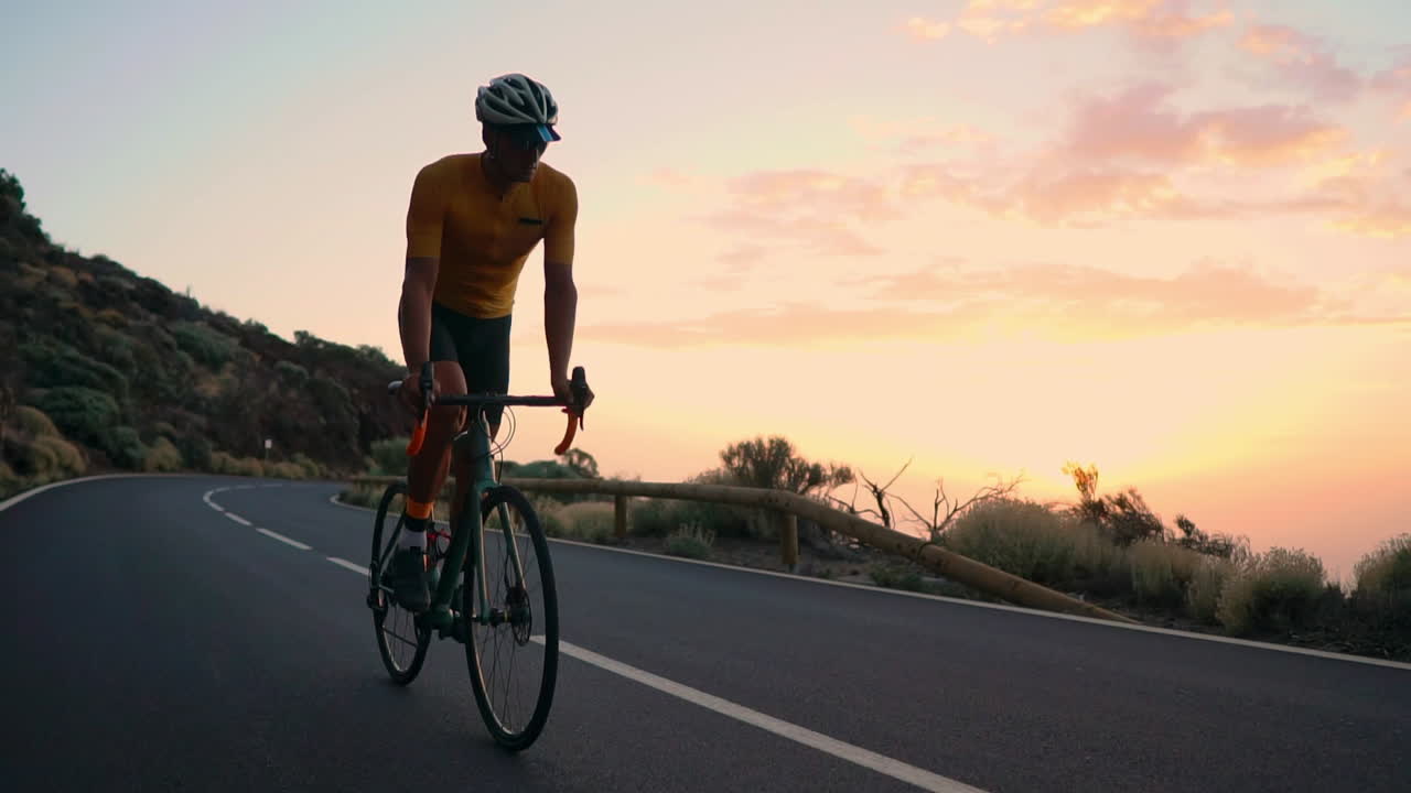 Captured in slow motion, the athlete cycles on a mountain serpentine, reveling in the island's view, representing a commitment to a healthy lifestyle at sunset