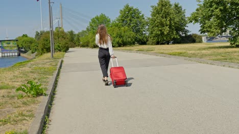 female tourist walking with red suitcase over empty road along river, riga