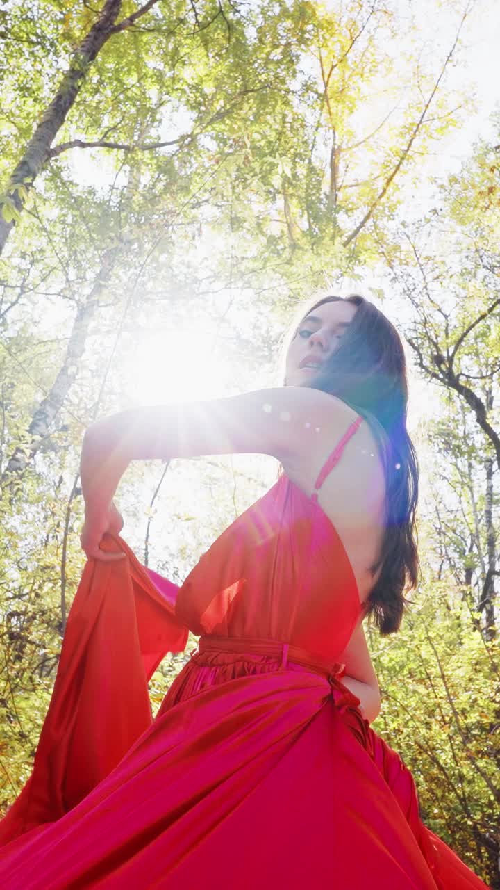 A Woman in a Flowing Red Dress Twirls Gracefully Among Sunlit Trees, Highlighting the Beauty of Nature and Fashion in a Magical Outdoor Setting