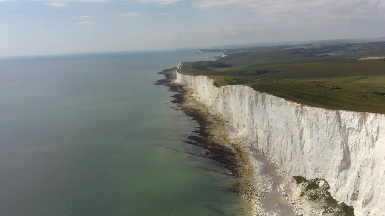 Aerial drone View of Beachy Head white chalk cliffs stretching along rugged coastline, with green fields above rocky shore and calm sea in Eastbourne England United Kingdom