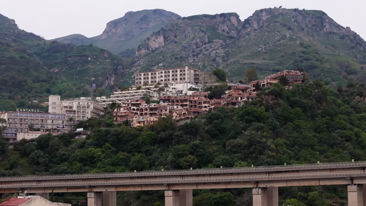 Aerial drone panning left shot revealing a hidden city on the mountain, surrounded by nature in Letojanni, near Taormina, Sicily, Italy (Sicilia, Italia)