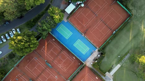 aerial top down rising above clay tennis courts and a professional golf course on a sport club at sunset