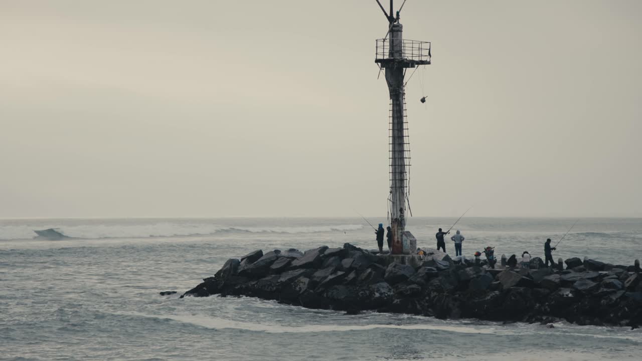 People Engaged in Fishing Along the Rocky Breakwater in Lima, Peru - Wide Shot