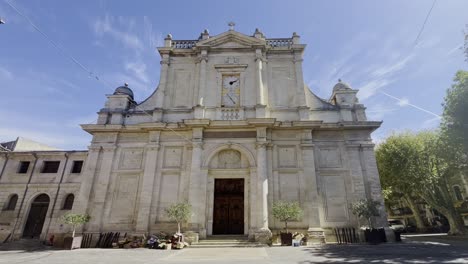 large house front of a church with stone columns and a large clock in strong sunshine in a historical place