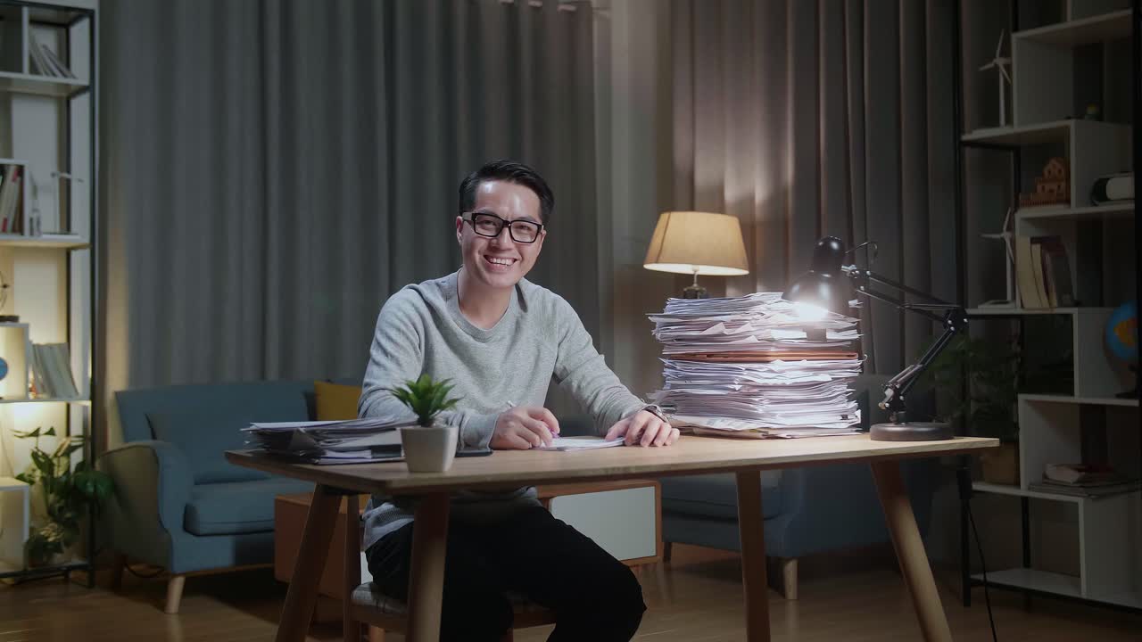 Asian Man Smiling To Camera While Working With Documents At Home