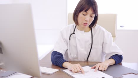 Worried female doctor looking at a computer and medical report