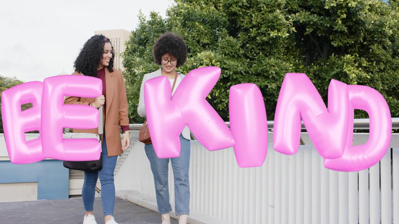 Due donne che si incontrano e poi camminano, chiacchierando mentre un "BE KIND" 3D rosa si sovrappone, promuovendo un messaggio sociale