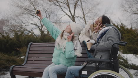 group of friends, two women and a disabled man in wheelchair, taking a selfie video at urban park during winter season 1