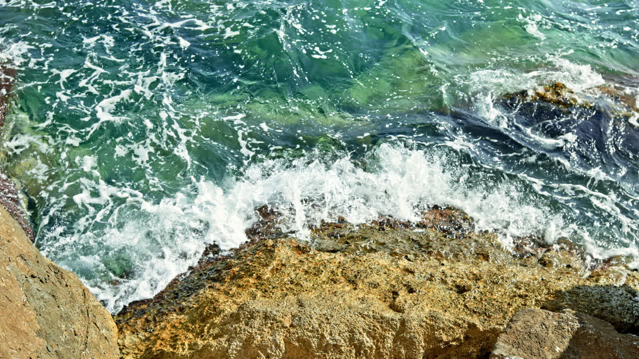 Le onde del mare formano schiuma mentre si infrangono contro le rocce. Costa oceanica rocciosa con acqua cristallina. Rocce nell'acqua