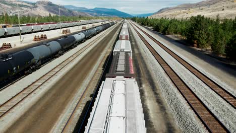 forward flight dolly drone shot flying over a cargo train on a railroad station in a desert environment on a sunny day next to a mountains in the background and powerines in the picture an tank trains