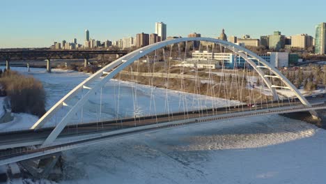 Luftaufnahme-Mit-Blick-Auf-Den-Weißen-Modernen-Gebundenen-Bogen-Futuristische-Walter-Dale-Überführung,-Die-Die-Hauptstadt-Edmonton-über-Dem-Eisigen,-Schneebedeckten-North-Saskatchewan-River-Trennt,-Sonniger-Winternachmittag-1-2