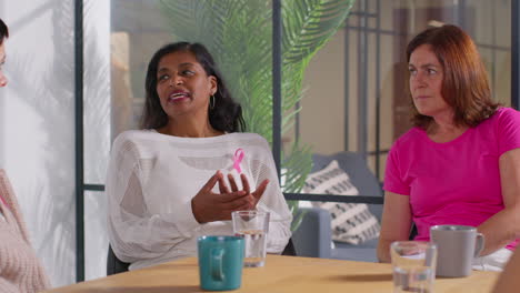 mature woman wearing pink breast cancer awareness ribbon talking at meeting of therapy support group for cancer treatment patients