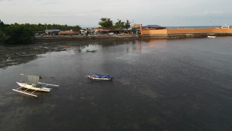 sweeping aerial view of taloot argao port during sunrise, with traditional double outriggers anchored near the coastline on reef in cebu, philippines