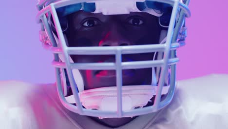 Video-of-close-up-of-african-american-american-football-player-over-blue-to-pink-neon-background