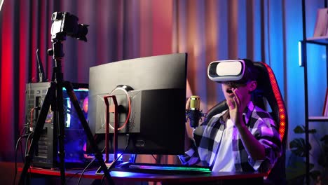 asian boy streamer playing game experience virtual reality in futuristic goggles. player touching air panel. personal computer on desk illuminated by rgb led strip light