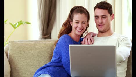 Happy-couple-sitting-on-the-couch-using-the-laptop