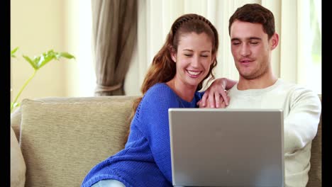 pareja feliz sentada en el sofá usando la computadora portátil