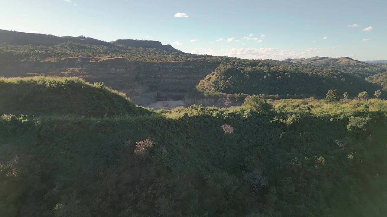 Un paesaggio di cava di calcare si dispiega vicino a Fercal, Brasília, Distretto Federale, Brasile Centro-Ovest, con un sorvolo in avanti di drone sopra un terreno minerario a cielo aperto terrazzato e un aspro bioma del cerrado durante l'ora d'oro.