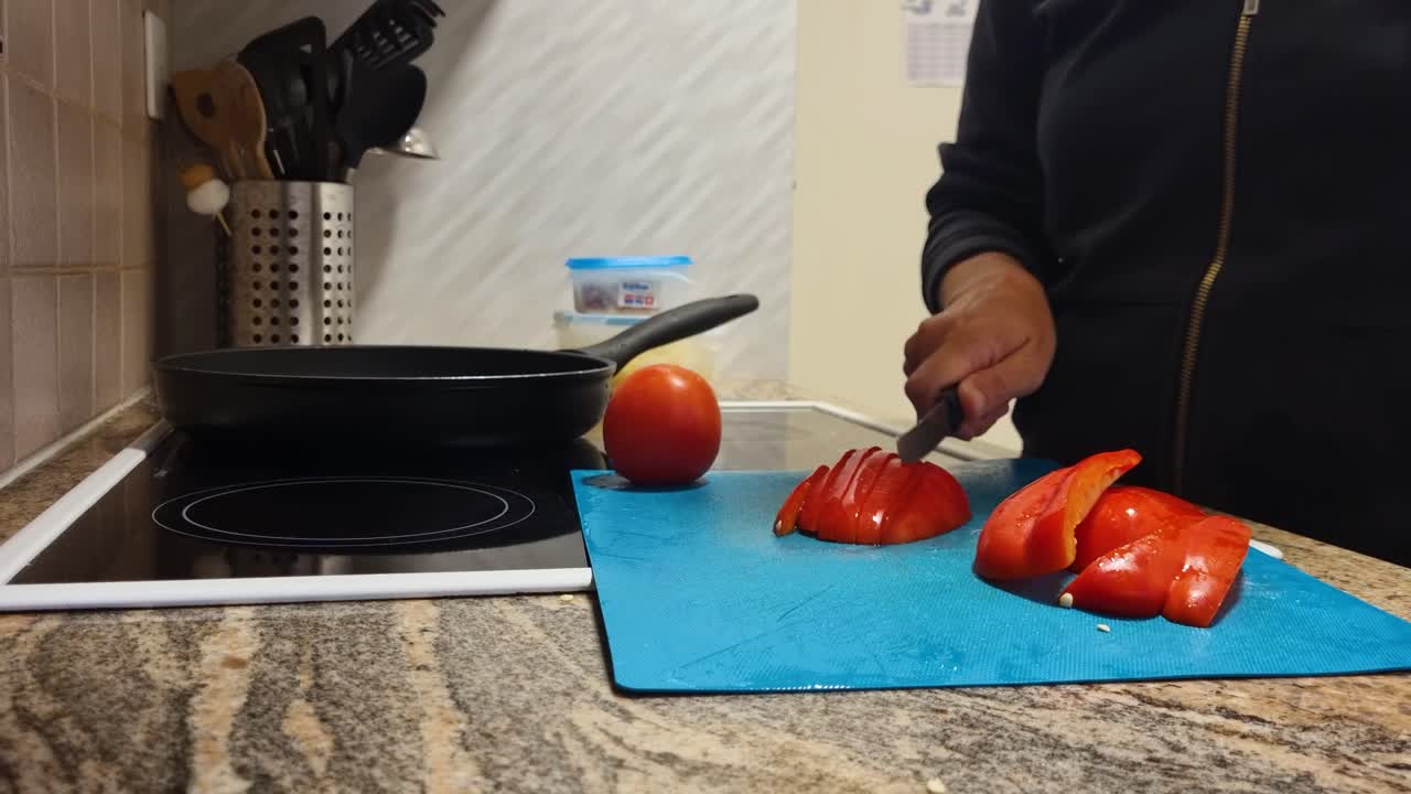 Close-up of a woman’s hands slicing shiny red bell peppers on a blue cutting board in her home kitchen, preparing a healthy vegetarian meal for her family, Swiss lifestyle