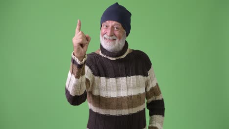 handsome senior bearded man wearing warm clothing against green background