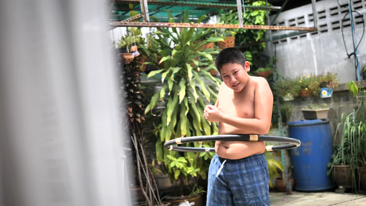 un chico gordo jugando al hula hoop en el patio trasero, en cámara lenta con el vientre moviéndose.