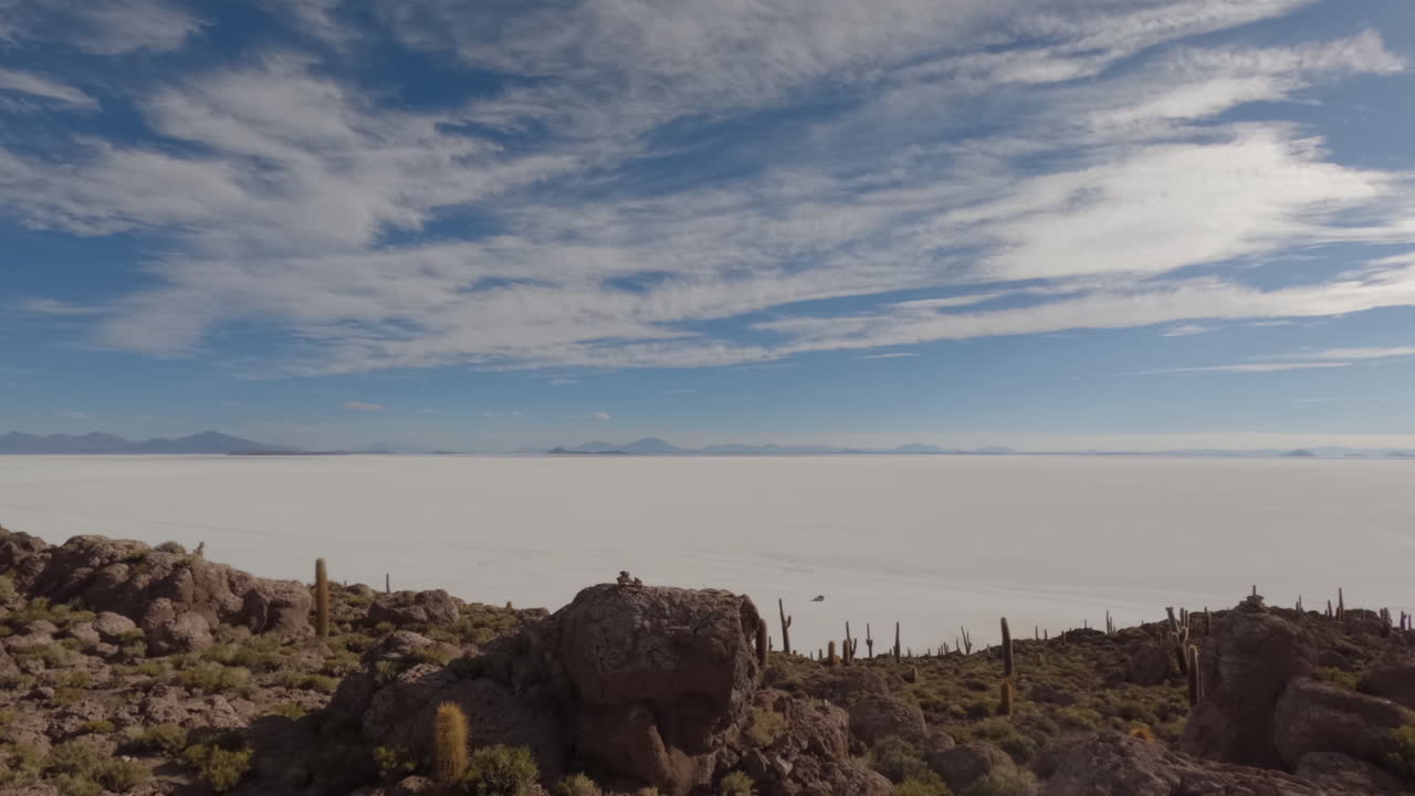 timelapse filmado desde la isla de cactus en medio de las llanuras de sal en bolivia en un día soleado con algunas nubes viendo sobre el amplio paisaje con cactus y rocas en primer plano