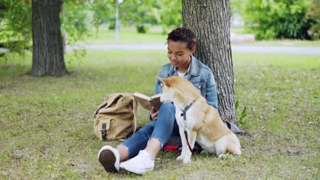 Teenage Girl Reading a Book in Park with Her Dog