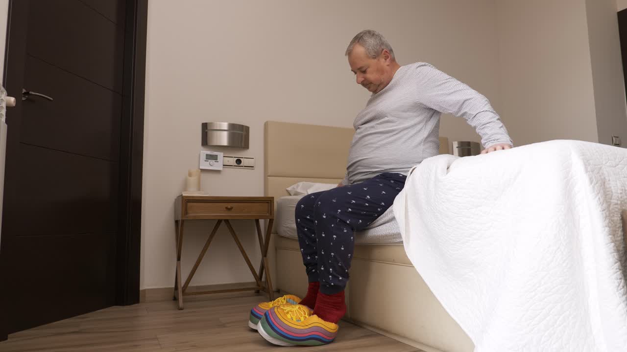 Aged man waking up and putting on funny slippers