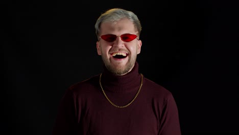 Smiling-stylish-young-man-in-red-sunglasses-looking-at-camera,-laughting-at-loud,-feeling-happiness