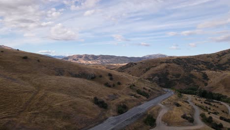 Drone-shot-following-vehicles-down-mountain-pass-on-dry-south-island,-new-zealand