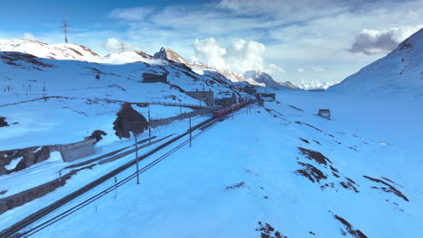 Red-passanger-train-speeding-up-after-leaving-Bernina-Ospizio-on-a-winter-evening-in-Switzerland