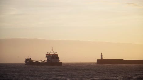 Fishing Trawler at Sea Next to Lighthouse at Sunset.