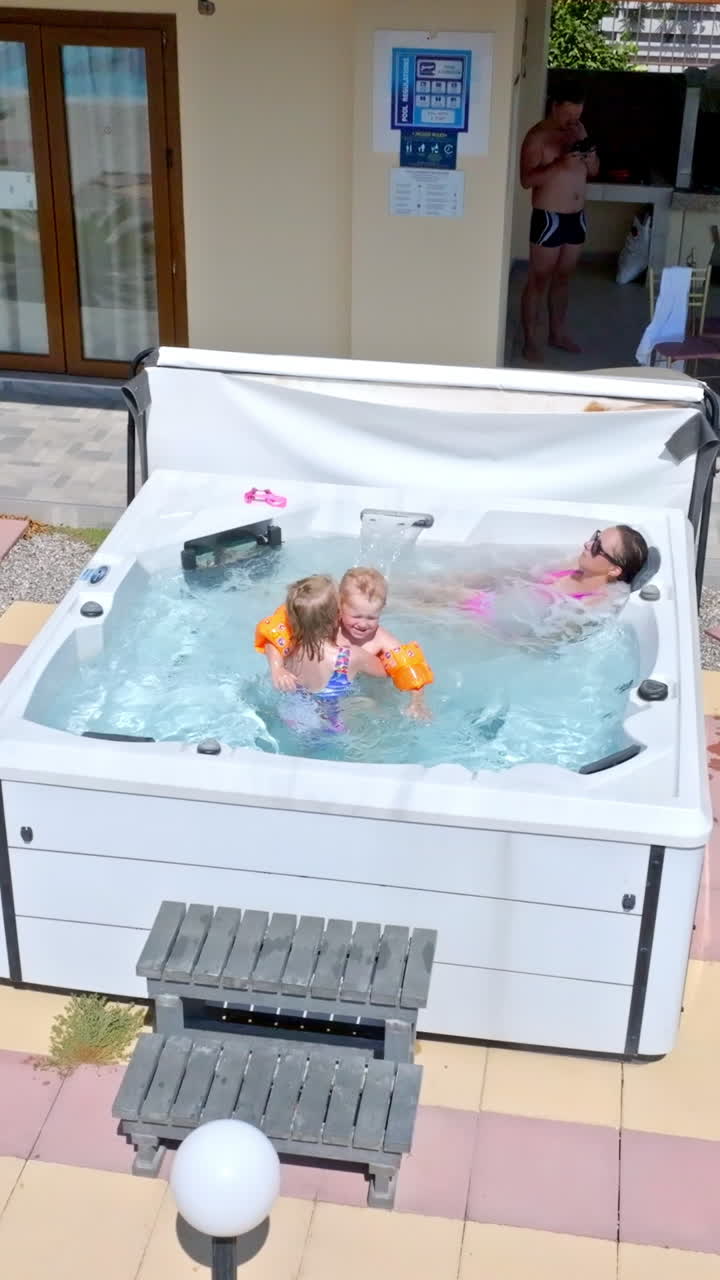Vertical drone shot of children hugging and mother enjoying a jacuzzi, sunny day
