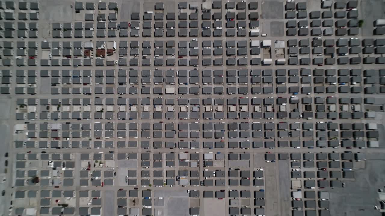 Pulling back aerial camera revealing flat-roof grid over subdivision, parked cars and growth