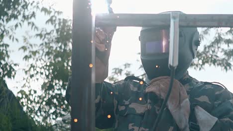 slow motion worker holds mask and welds parts of fence