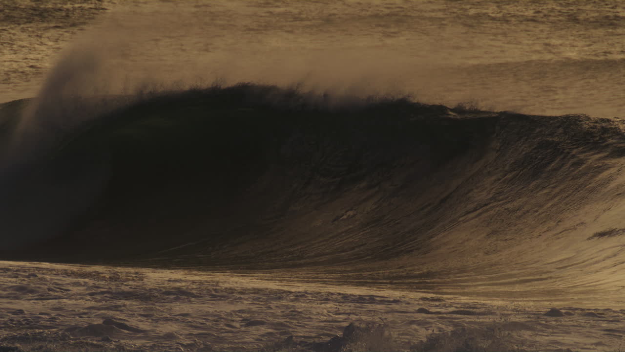 A stunning slow-motion capture of a wave at sunset, filmed from the shore, showcasing the dark silhouette of the wave against the glowing horizon