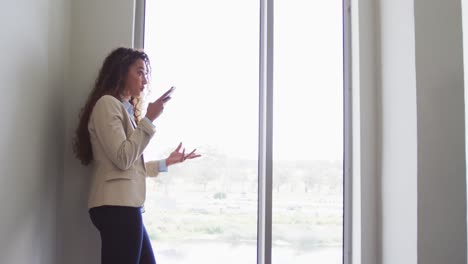 mujer de negocios biracial sonriendo y hablando en un teléfono inteligente en interiores modernos