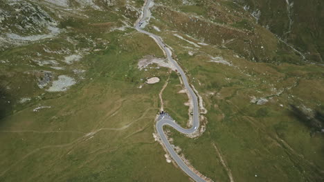 Top-down-aerial-shot-capturing-a-serpentine-road-winding-through-the-verdant-landscapes-of-Transalpina-in-Romania,-with-patches-of-rocks-and-water-streams-visible