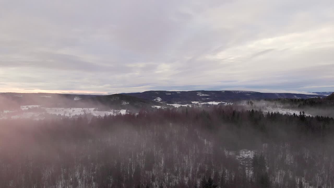 Drone flying through fog over snowy forest in Sweden with sun shining from the side
