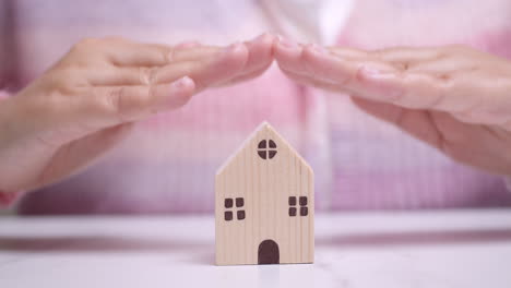 manos flotando sobre una pequeña casa de madera manifestando el deseo de poseer una casa y mucha propiedad inmobiliaria