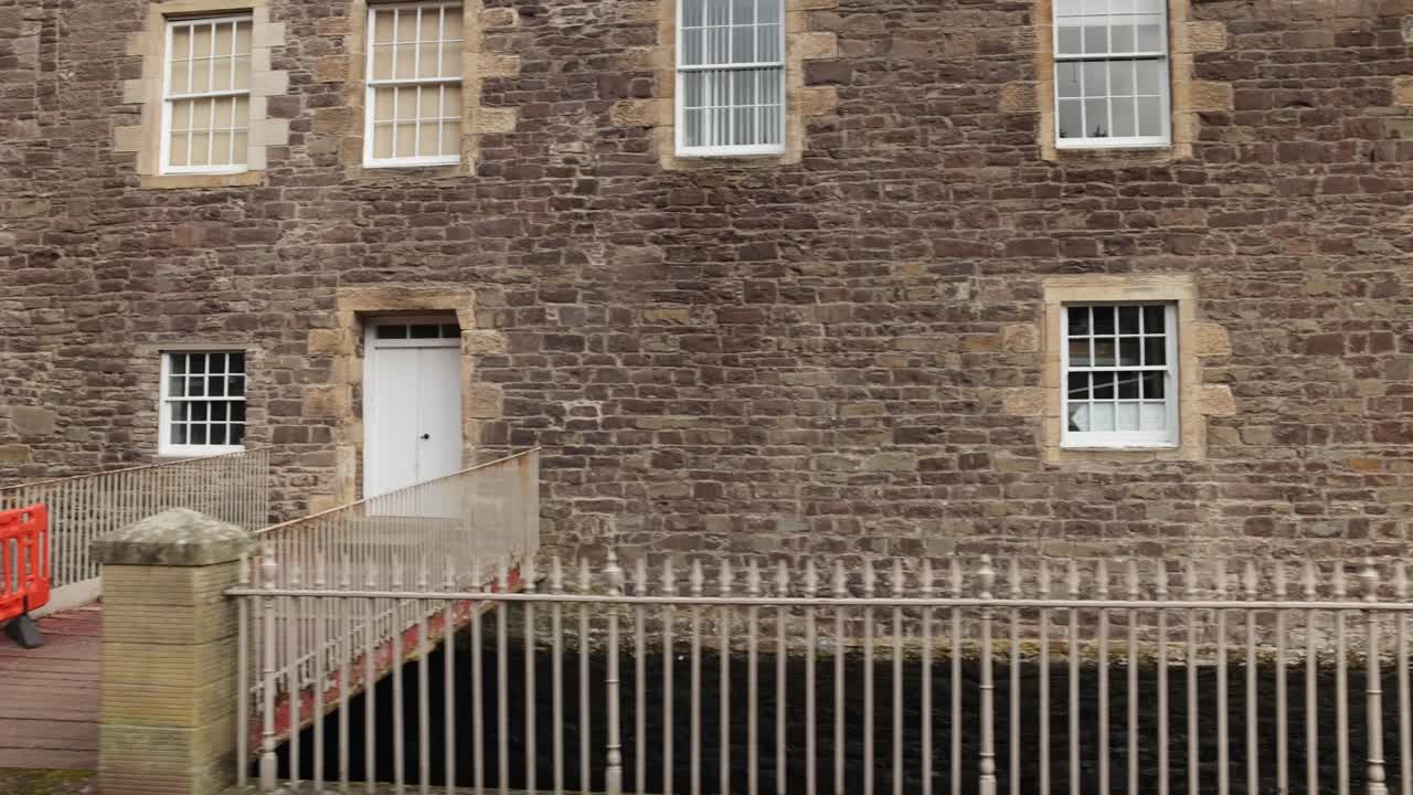 Slow dolly shot along antique buildings within New Lanark with signs