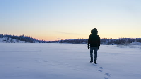 aerial of person walking on snowy frozen lake in wilderness, canada