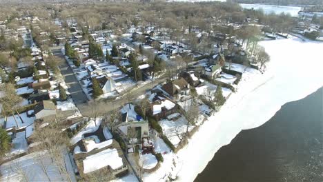 Drone-Aéreo-Sobre-Casas-Cubiertas-De-Nieve-Zona-Residencial-En-Una-Orilla-Del-Río