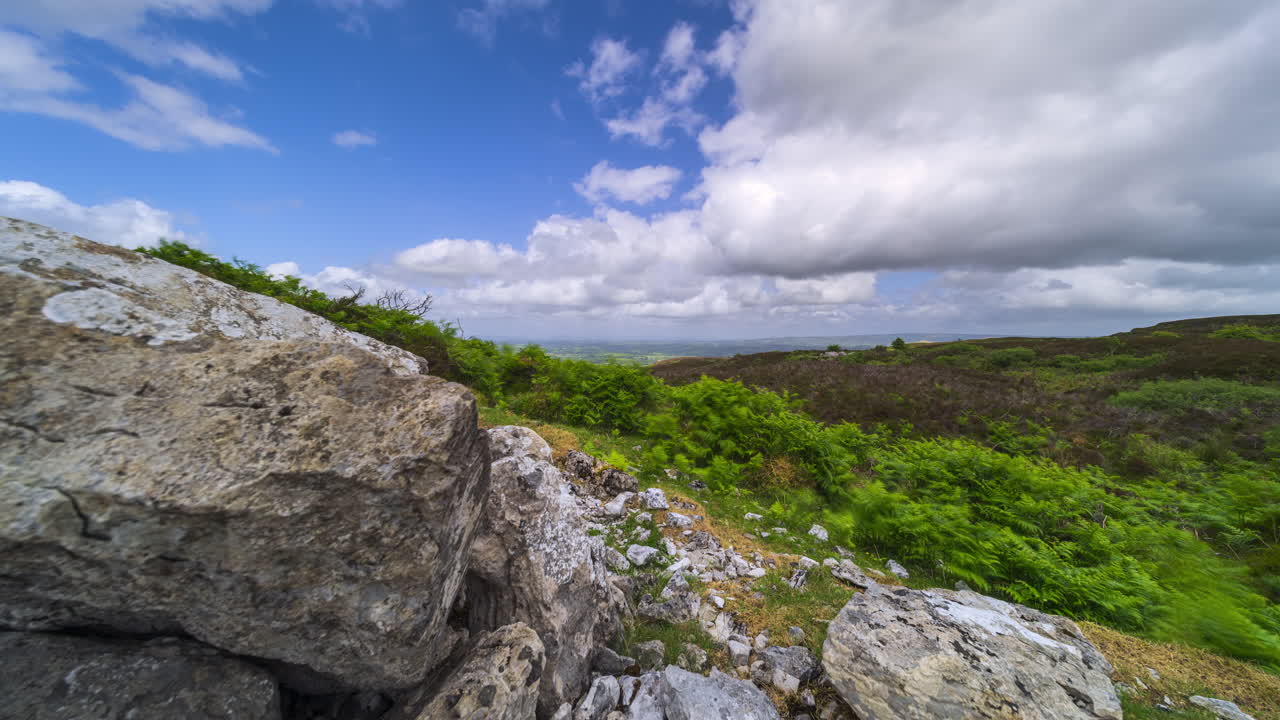 Timelapse di un paesaggio rurale con una formazione rocciosa in primo piano e colline in lontananza durante una giornata nuvolosa e soleggiata, visto da Carrowkeel nella contea di Sligo in Irlanda