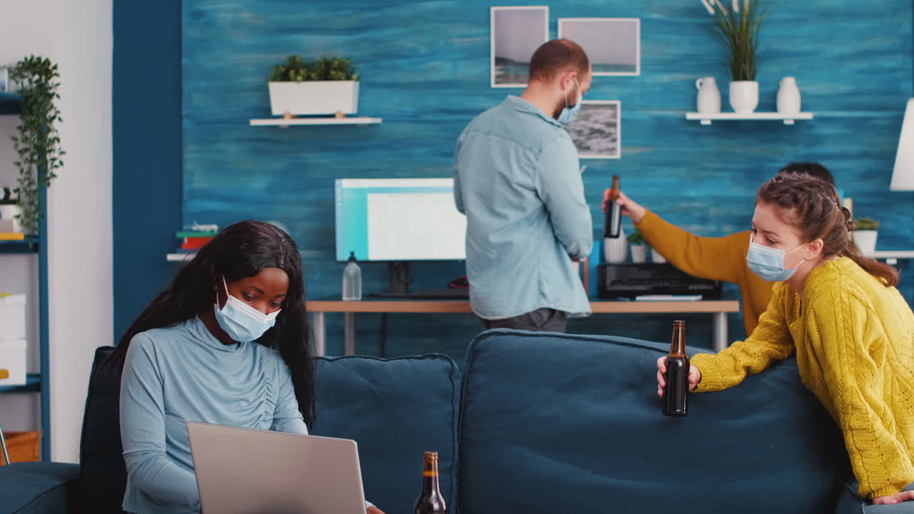 African woman with face mask pointing on laptop sitting on sofa