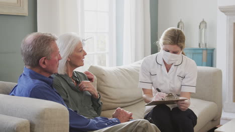 female doctor with mask makes home visit to senior couple for medical check during covid-19 lockdown