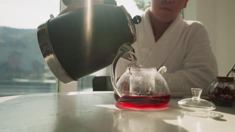 el hombre llena gradualmente la tetera para preparar té de frutas. el joven usa la tetera de la tetera y la mezcla de té natural para preparar una bebida saludable por la mañana